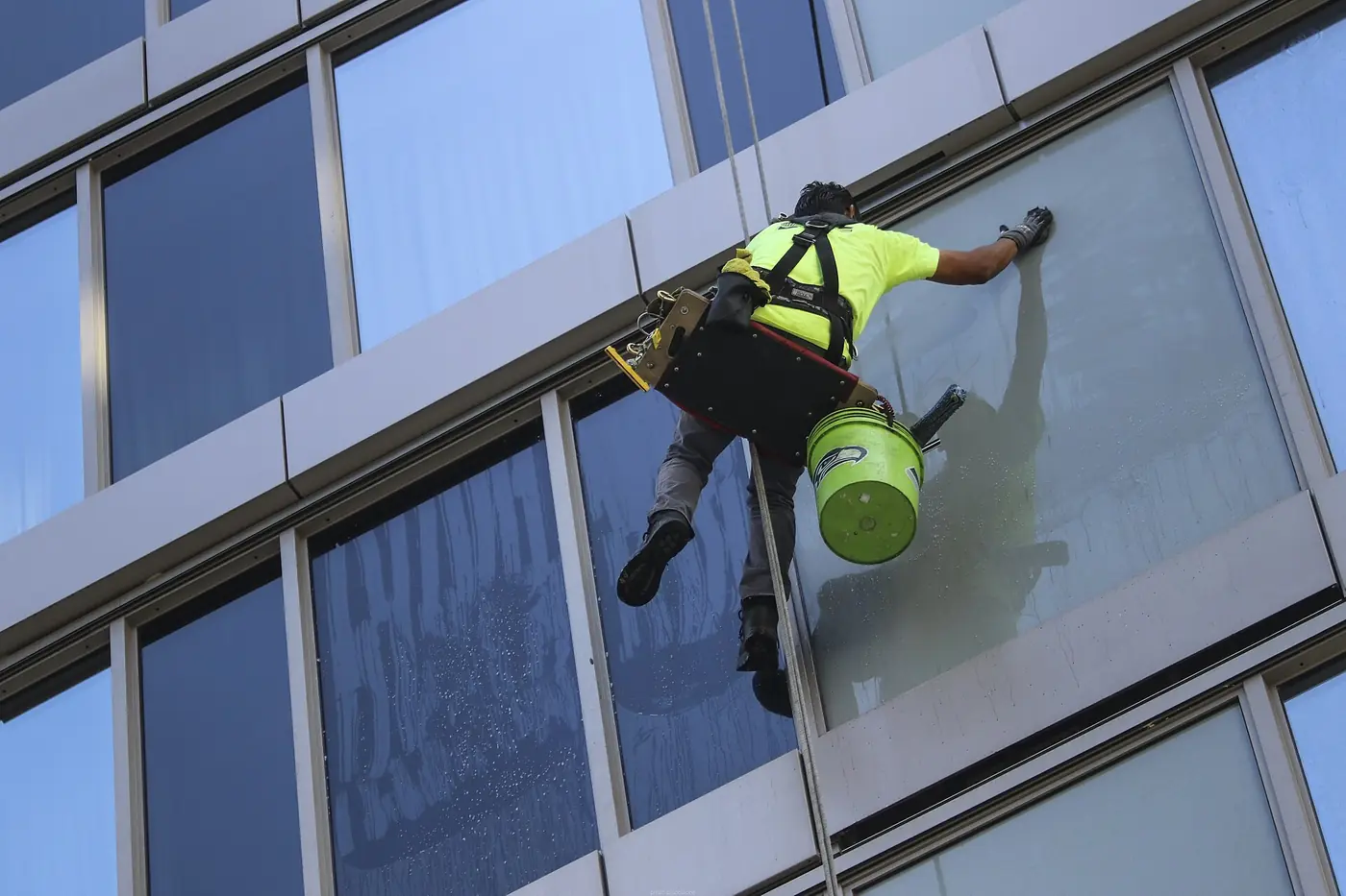 Laveur de vitres suspendu à une façade vitrée, en tenue jaune haute visibilité